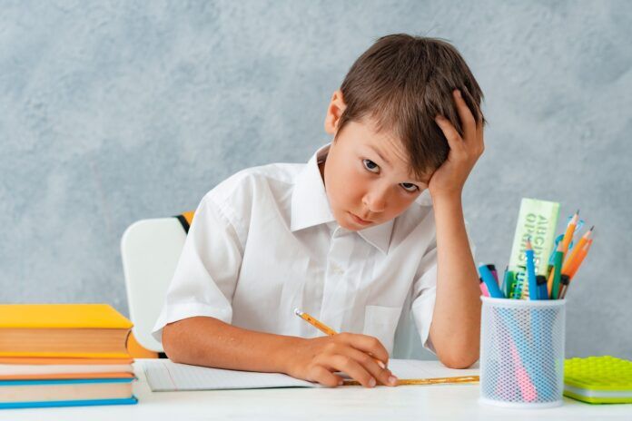 Back to school. Happy smiling student draws at the Desk. A schoolboy solves his homework. A boy from elementary school Mācības
