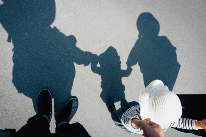 Shadow on gravel path of a loving family of three holding hands walking outdoors on a lovely sunny day